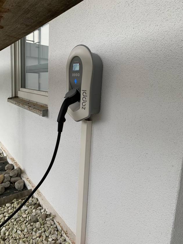 Wandmontierte Ladestation mit eingestecktem Ladekabel an einem Gebäude in Warthausen.